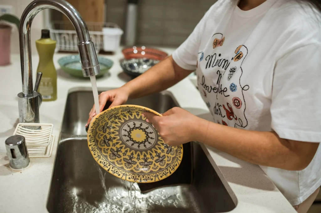 Person washing a bowl with soap and warm water in a kitchen sink