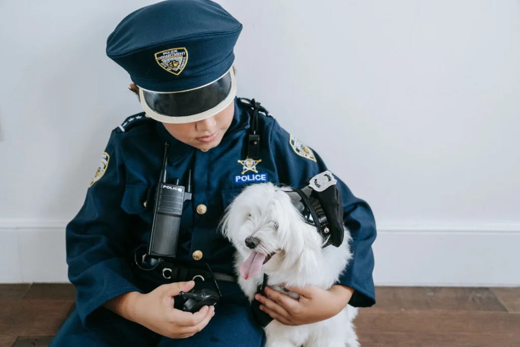 Child in a police officer Halloween costume hugging a small white fluffy dog